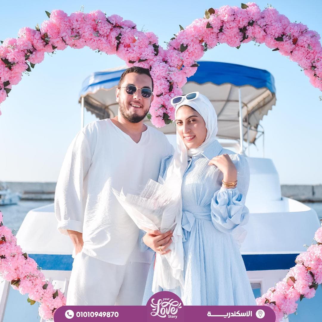 زوجان يبتسمان على متن قارب في الإسكندرية، داخل إطار من الزهور الوردية على شكل قلب.